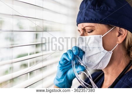 Stressed Female Doctor or Nurse On Break At Window Wearing Medical Face Mask and Goggles.