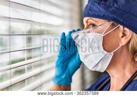 Female Doctor or Nurse On Break At Window Wearing Medical Face Mask and Goggles.