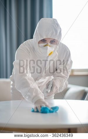 Woman In White Workwear And Protective Gloves Looking Concentrated While Disinfecting The Table Surf