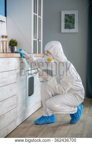 Woman In White Workwear And Protective Gloves Disinfecting The Room