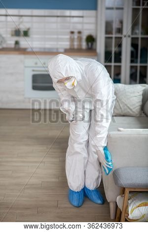 Woman In White Workwear And Protective Eyeglasses Disinfecting Furniture