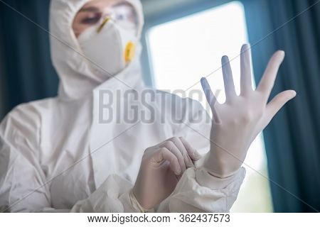 Woman In White Workwear Looking At Her Hand In A Protective Glove