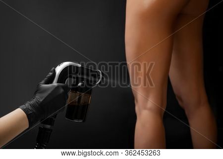Cosmetology Professional Applying Liquid Tan Spray On Woman Skin With Aerograph On Black Background
