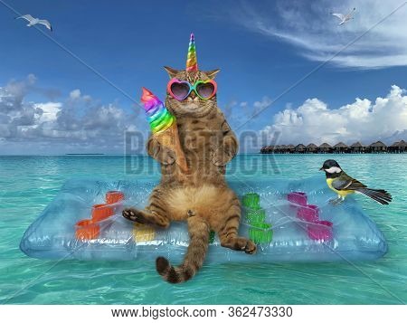 The Beige Cat Unicorn In A Heart Shaped Sunglasses With A Rainbow Ice Cream Cone Is Relaxing On A Bl