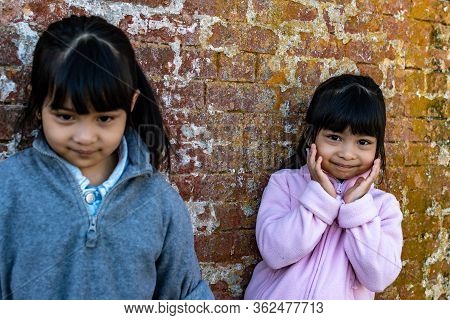 Asian Identical Female Twins Child Wearing Jacket During Cold Weather And Standing On An Old Brick W