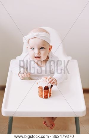 Cute Baby In A Baby Chair Enjoys Eating The Cake With His Hands. Baby With A Birthday Cake On White 