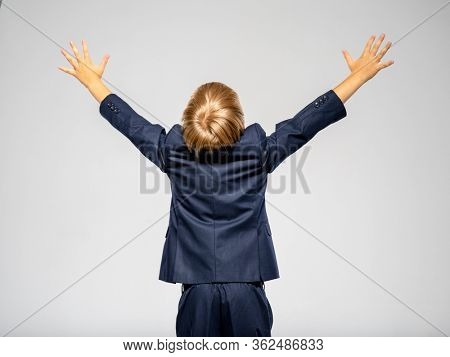 Photo of a businessman boy with raised hands up - isolated. Back view of white   kid in a blue business suit looking up.  Boy dressed in a formal suit with hands up, rear view