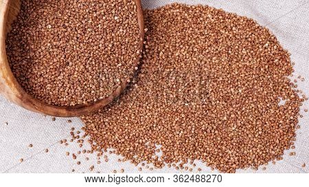Raw Roasted Buckwheats From Round Wooden Bowl Pour On Cloth Surface. Russian Grechka. Organic Health