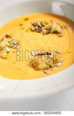 Pumpkin soup in white bowl. Served main course close up. Vegetable cream soup decorated with seeds. Restaurant food portion, main course. Vegetarian supper. Dinner, gourmet meal in plate