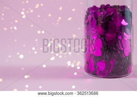 Glass Bottle With Purple Heart Shaped Sparkles On Pink Background With Copy Space And Blurred Lights