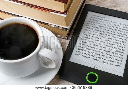 Close-up Of E-book Reader Near Cup Of Hot Coffee And Stack Of Ordinary Paper Books. Copy Space On E-