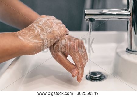 Hand washing personal hygiene woman washing hands rubbing soap for 20 seconds following steps, cleaning wrists and rinsing under water at home bathroom. COVID-19 infection prevention handwashing.