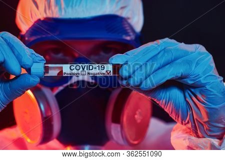 COVID-19 or 2019-nCoV. Close-up portrait of a scientist microbiologist in a protective PPE suit showing the coronavirus test tube. Vaccination.