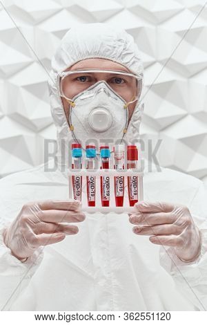 COVID-19. Doctor, microbiologist, scientist in a protective suit, shows test tubes with blood samples of infected people on a white background. Coronavirus test.