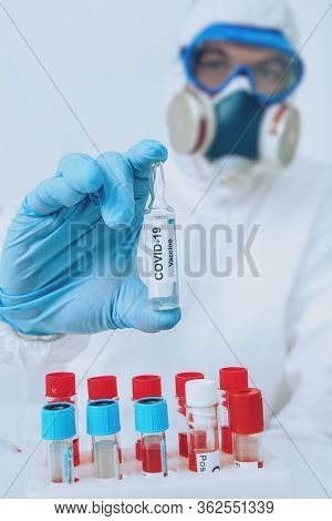 COVID-19 or 2019-nCoV. Doctor microbiologist scientist in a protective PPE suit shows the ampoule with a vaccine against coronavirus. Vaccination.