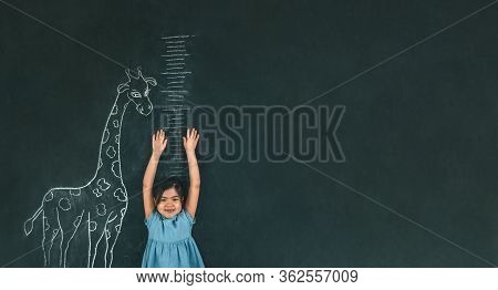 A Girl Measures Her Height Against A Dark Board With A Picture Of A Giraffe