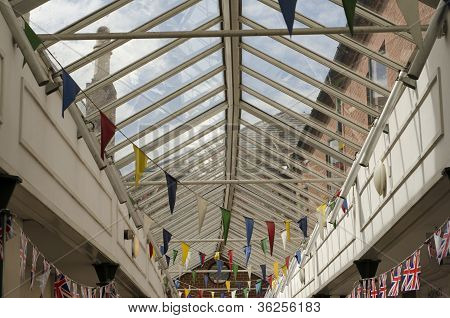 Colourful Bunting Flags In A Glass Roofed Walkway In An English Town.
