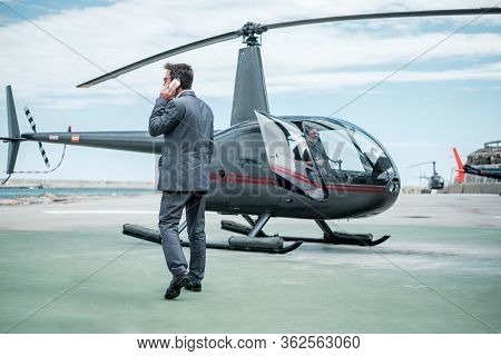 Businessman talking over the phone near private helicopter