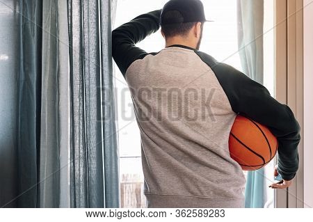 Man Confined Looking Out His Window With A Basketball, Concept Of Quarantine And Confinement