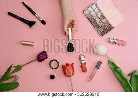 Girl Holds Makeup Brush Set Of Cosmetics And Flowers On Pink Background