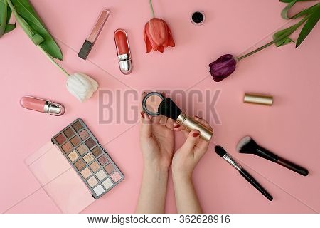 Girl Holds Makeup Brush Set Of Cosmetics And Flowers On Pink Background