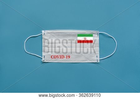 Medical Mask With The Flag Of Iran And The Inscription Covid-19 On A Blue Background