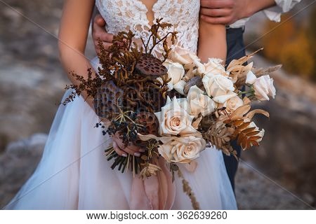 Wedding Decorations. The Groom Hugs The Bride, Who Is Dressed In A White Wedding Dress And Is Holdin