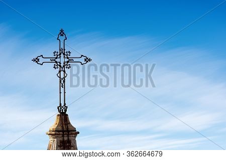 Closeup Of An Ancient Christian Cross In Wrought Iron On A Blue Sky With Clouds And Copy Space. Metr
