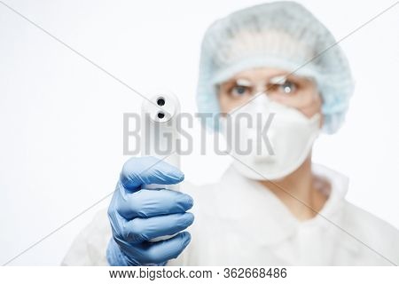 Close-up shot of doctor wearing PPE protective suit and surgical mask using infrared forehead thermometer or thermometer gun to check body temperature for virus symptoms - coronavirus outbreak concept