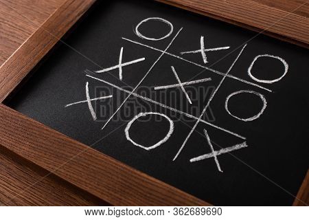 Tic Tac Toe Game On Blackboard With Chalk Grid, Naughts And Crosses On Wooden Surface