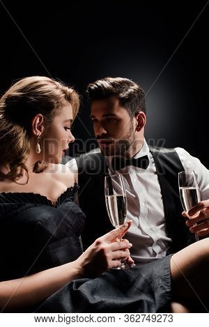 Sexy Woman And Elegant Man Holding Glasses Of Champagne And Looking At Each Other On Black Backgroun