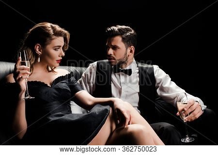 Elegant Man And Woman Sitting On Leather Sofa With Glasses Of Champagne And Looking At Each Other Is