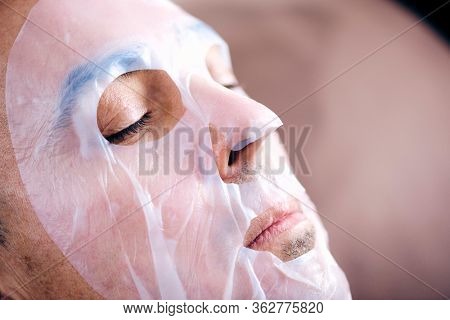 closeup of a handsome caucasian man wearing a bio-cellulose sheet mask while is relaxing