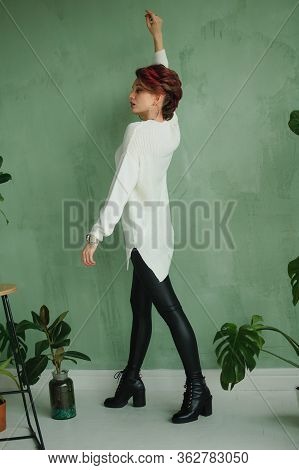 Back View Of Sensual Young Girl In White Sweater And Black Leather Leggings Possing At Studio With G