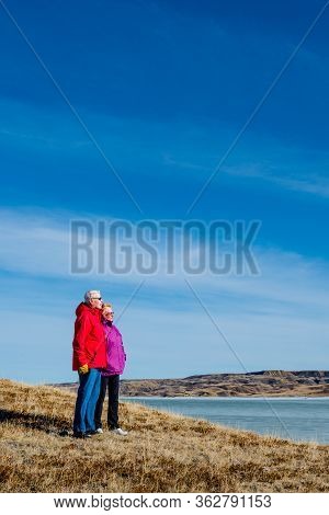 Senior Couple Standing Overlooking An Ice-covered Lake Diefenbaker