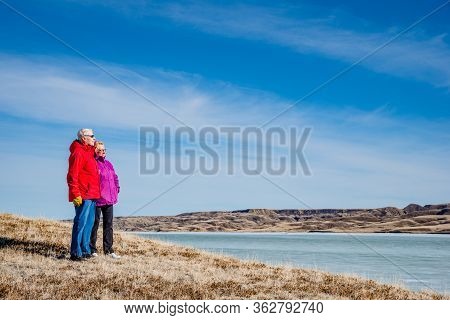Senior Couple Standing Overlooking An Ice-covered Lake Diefenbaker