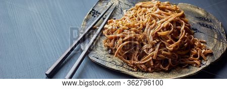Buckwheat Noodle With Teriaki Sauce. Asian Dish. With Wooden Sticks. On A Clay Plate And A Gray Back