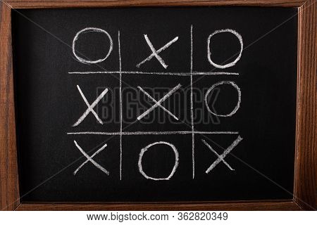 Top View Of Tic Tac Toe Game On Blackboard With Chalk Grid, Naughts And Crosses