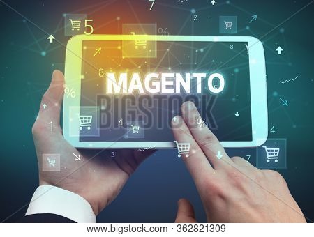 Close-up of a hand holding tablet with MAGENTO inscription, online shopping concept