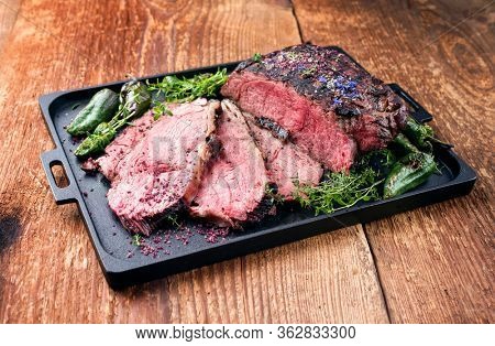 Traditional Commonwealth Sunday roast with sliced cold cuts roast beef with herbs and chili as closeup on a modern design tray 