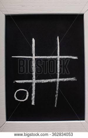 Top View Of Tic Tac Toe Game On Blackboard With Chalk Grid And Naught On Wooden Surface