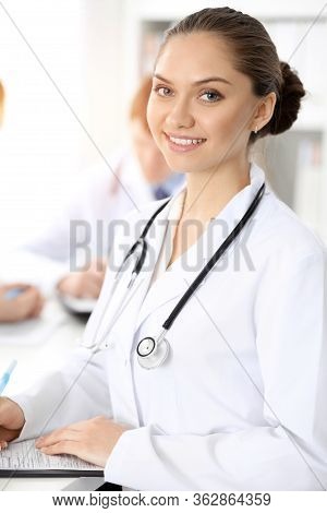Happy Smiling Woman-doctor Sitting And Looking At Camera At Meeting With Medical Staff . Medicine Co