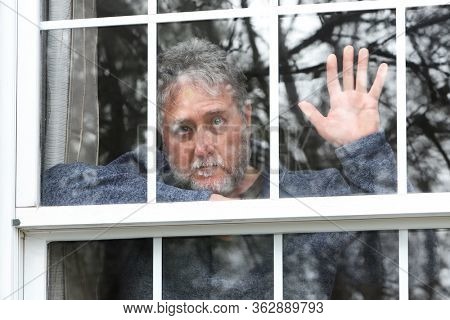 Bearded man stuck in quarantine with his hand up at the window