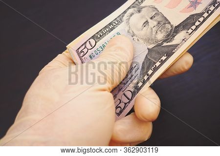 A Hand In A Flesh-colored Latex Glove Holds A Bundle Of American Us Money. Above Is A 50 Dollar Bill