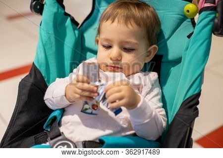 Sweets For Children Concept. Little Cute Hungry Baby Girl Sitting In A Stroller And Eating A Lozenge