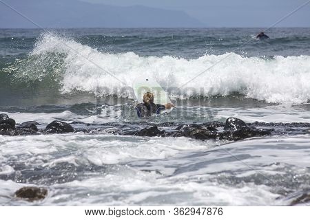 The Surf Enters The Water. Male Surfer Entering The Sea With His Board In A Black Surfing Suit. Tene