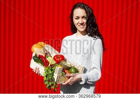 Woman With A Box Of Vegetables On A Red Background. Fresh Vegetables In The Box. Young Woman With Fi