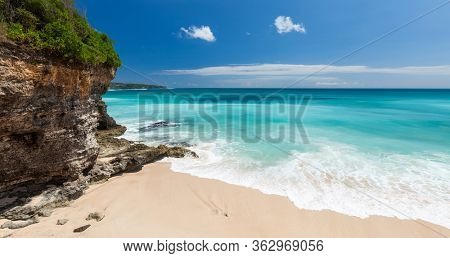 Balinese sandy beach with green steep cliff and torquoise water. Bali, Indonesia