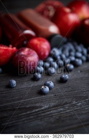 Mix of fresh red and black fruits. With botteled fresh juices. Placed on black wooden table.