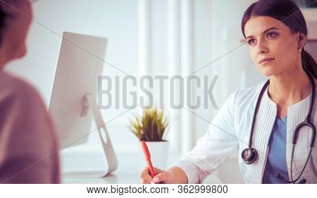 Doctor and patient discussing medical problems in a hospital consulting room. Doc filling in a patient's form